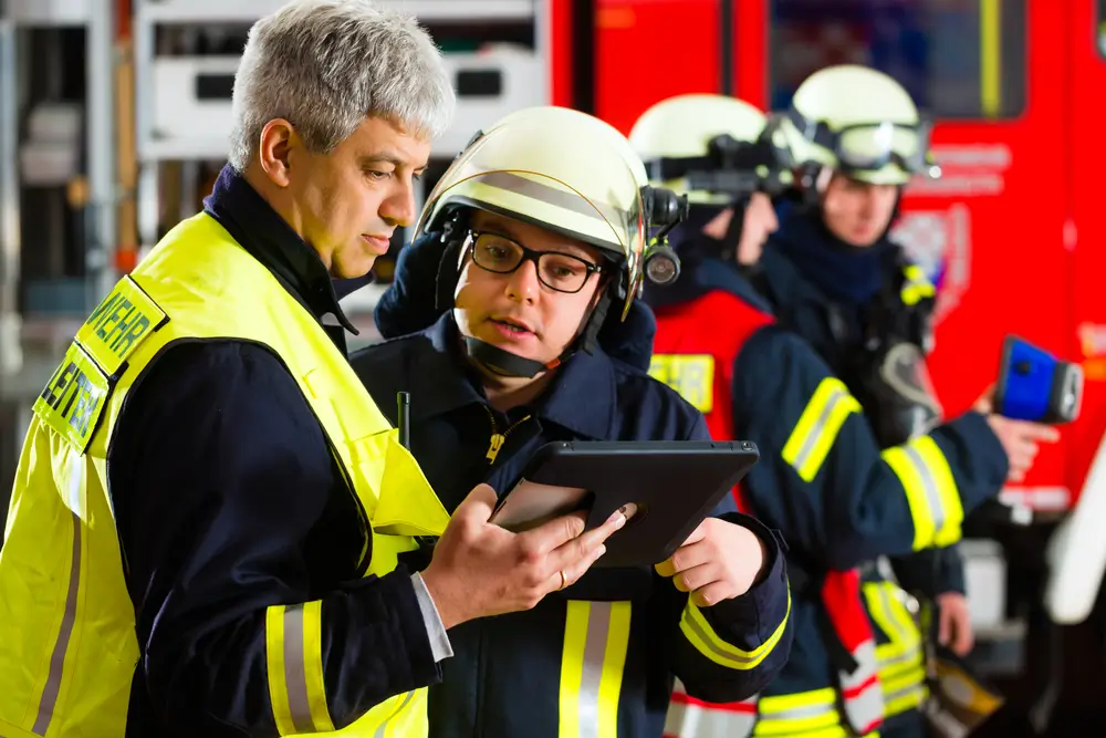 Sapeurs-pompiers consultant un manuel de formation sur tablette pour préparer leur avancement de grade.