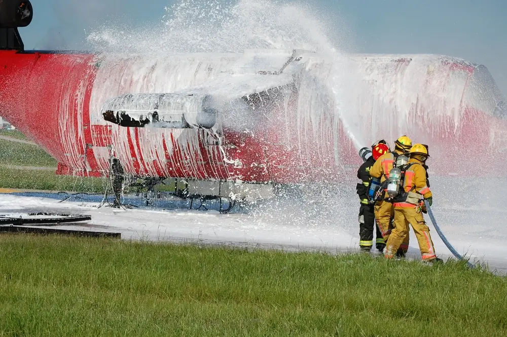 Équipe de pompiers d'aéroport projetant de la mousse sur un avion lors d'un exercice de sécurité incendie.