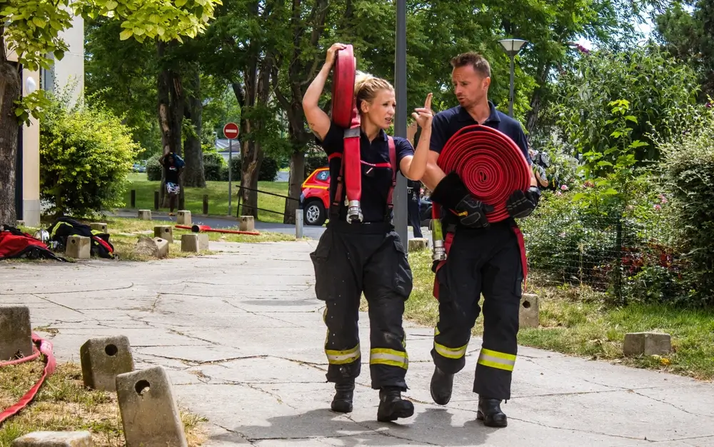 Recrues pompiers portant de lourds tuyaux lors d'un test d'aptitude physique pour l'engagement volontaire.