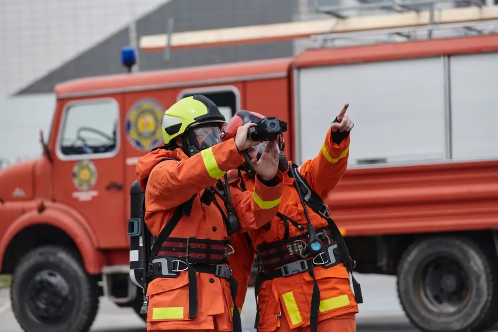 Officier pompier chef d'agrès coordonnant une intervention avec une caméra thermique devant un camion de pompiers.