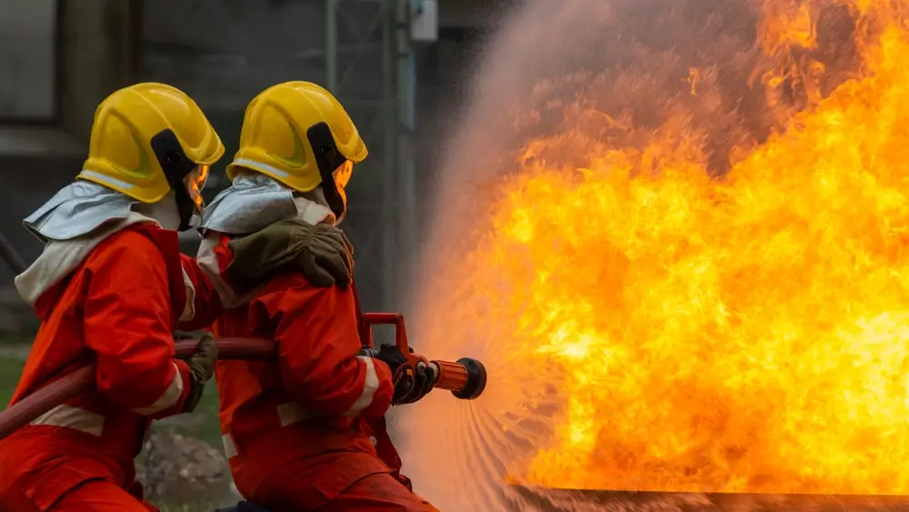 Sapeurs-pompiers professionnels en intervention utilisant une lance à incendie face aux flammes.