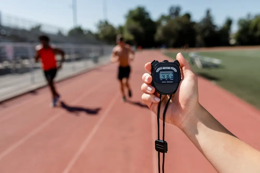 Chronomètre tenu à la main sur une piste d'athlétisme pour mesurer la performance de coureurs à l'entraînement.