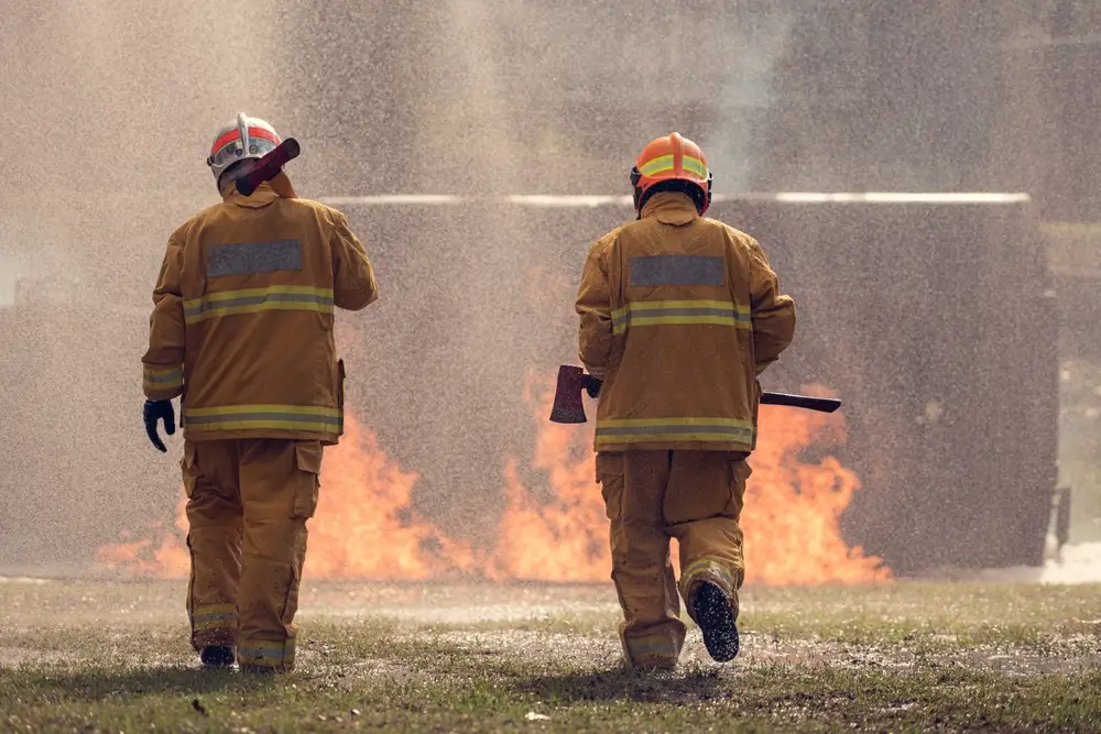 Deux pompiers en tenue ignifugée s'approchent de flammes lors d'un exercice d'entraînement incendie.