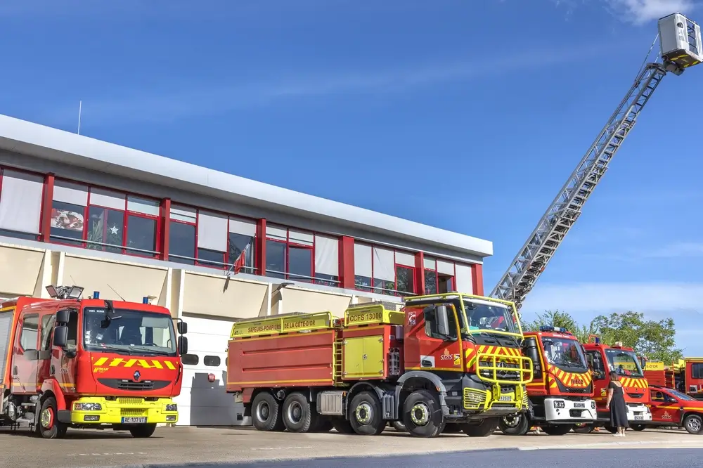 Plusieurs camions de pompiers stationnés devant une caserne avec une grande échelle télescopique déployée.