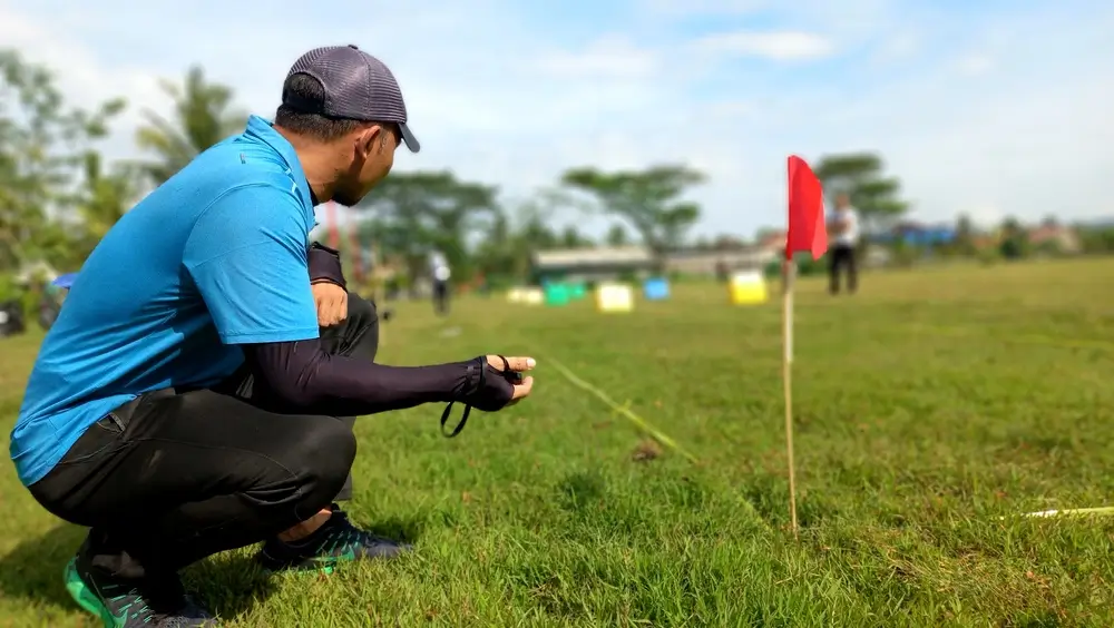 Entraîneur accroupi avec un chronomètre pour une évaluation physique d'endurance cardio-respiratoire en plein air.