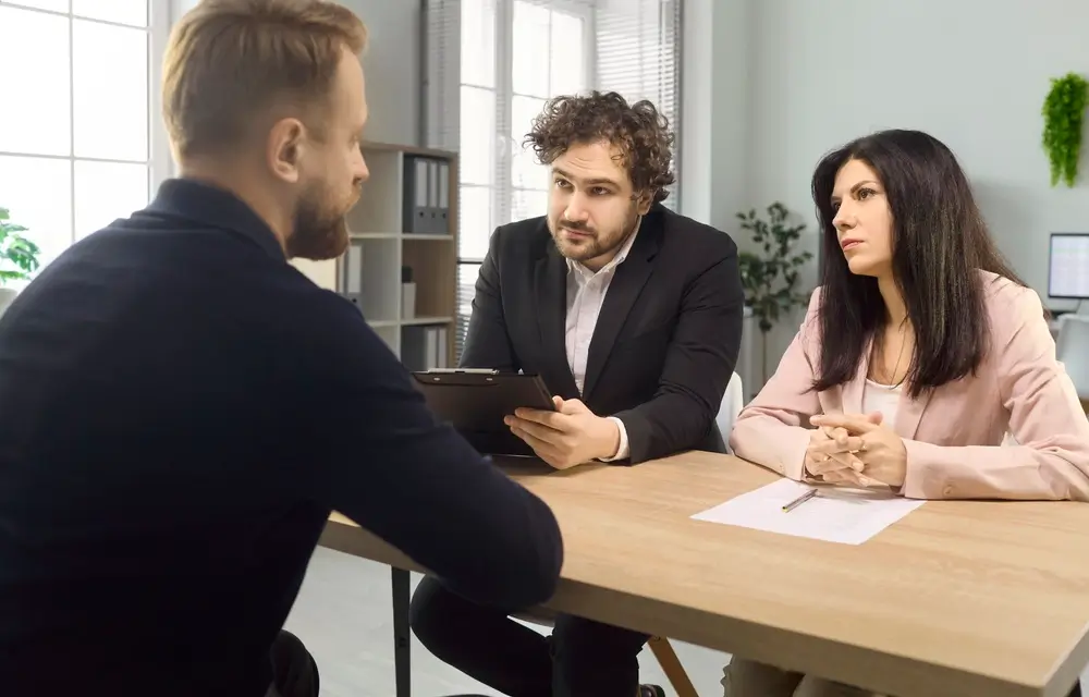 Candidat de dos face à un jury attentif composé d'un homme et d'une femme lors d'un entretien oral de recrutement.